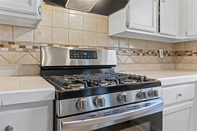 kitchen featuring stainless steel gas range oven, white cabinetry, exhaust hood, light countertops, and decorative backsplash