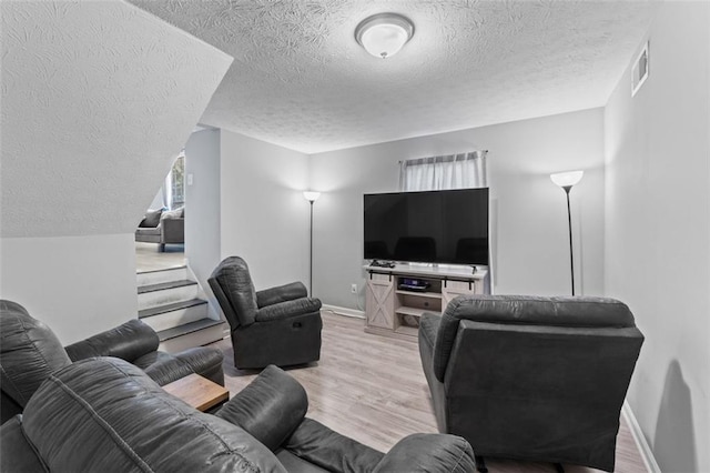 living area featuring visible vents, a textured ceiling, baseboards, and wood finished floors