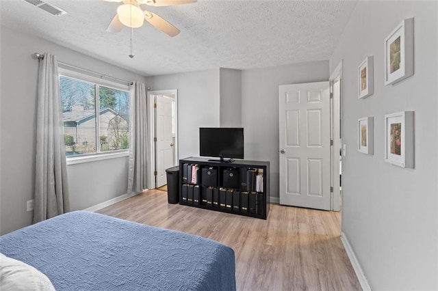 bedroom featuring visible vents, baseboards, wood finished floors, a textured ceiling, and a ceiling fan