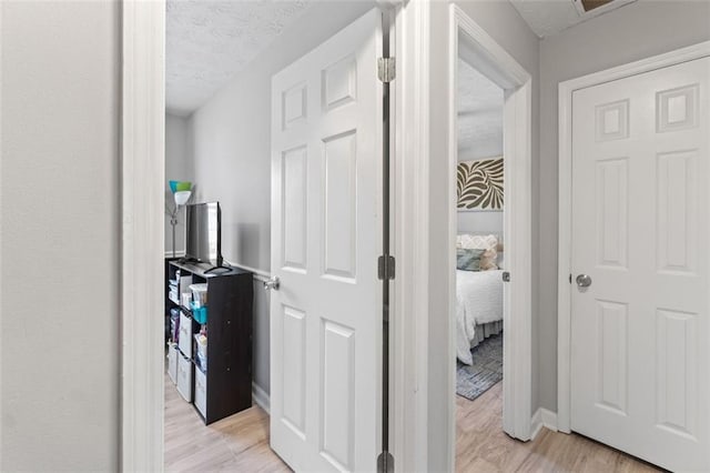 corridor featuring baseboards, a textured ceiling, and light wood-style floors