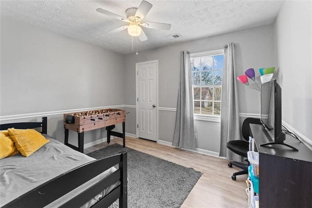 bedroom with visible vents, ceiling fan, baseboards, wood finished floors, and a textured ceiling