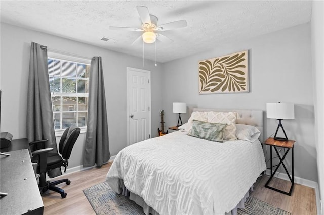 bedroom with visible vents, baseboards, light wood-type flooring, a textured ceiling, and a ceiling fan