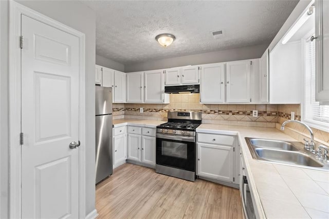 kitchen featuring light wood-style flooring, a sink, white cabinets, under cabinet range hood, and appliances with stainless steel finishes