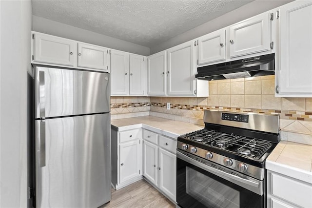 kitchen with under cabinet range hood, decorative backsplash, appliances with stainless steel finishes, and white cabinets