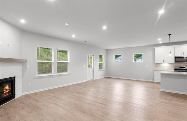 unfurnished living room with a fireplace, baseboards, light wood finished floors, and recessed lighting