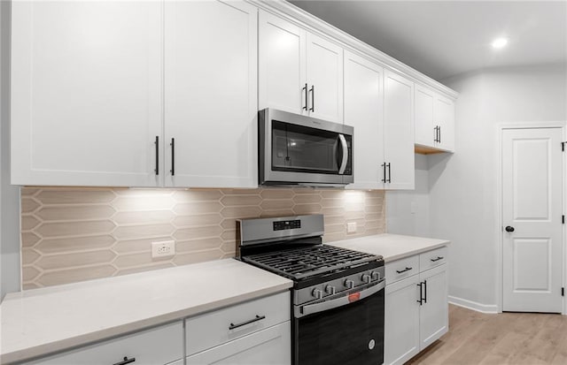 kitchen with light countertops, stainless steel appliances, white cabinetry, light wood-type flooring, and backsplash