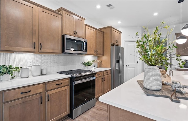 kitchen with appliances with stainless steel finishes, tasteful backsplash, hanging light fixtures, light countertops, and light wood-style floors