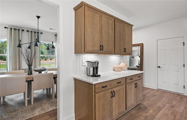 kitchen featuring light countertops, dark wood finished floors, brown cabinetry, backsplash, and visible vents