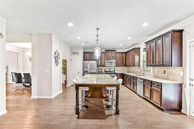 kitchen featuring a sink, dark brown cabinets, appliances with stainless steel finishes, a kitchen bar, and tasteful backsplash