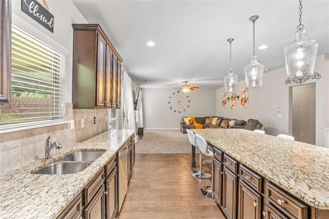 kitchen with a sink, backsplash, open floor plan, pendant lighting, and stainless steel dishwasher