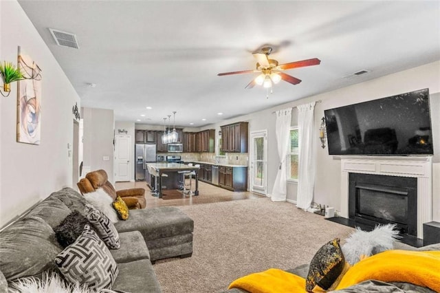 living area with light carpet, a fireplace with flush hearth, visible vents, and ceiling fan