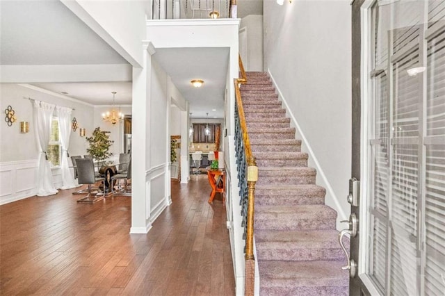 entryway with stairway, hardwood / wood-style floors, wainscoting, an inviting chandelier, and a decorative wall