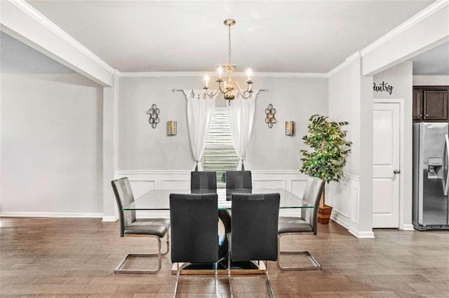 dining space with wood finished floors, an inviting chandelier, wainscoting, crown molding, and a decorative wall