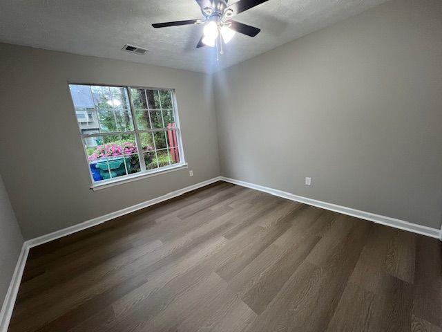 unfurnished room featuring baseboards, visible vents, ceiling fan, and dark wood finished floors
