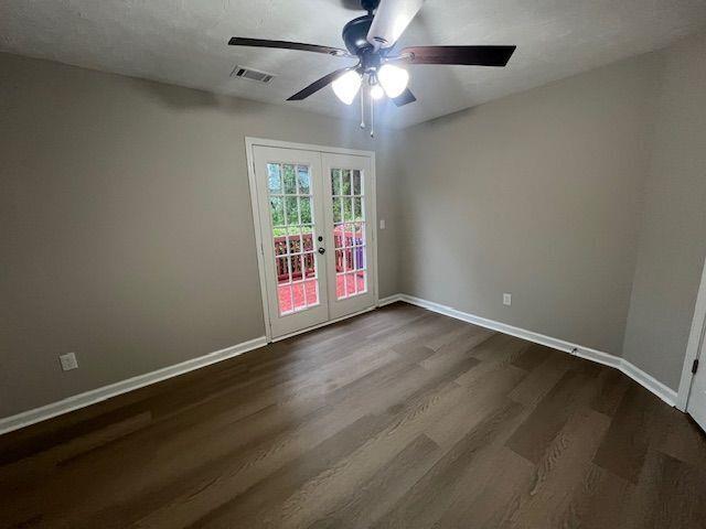 spare room featuring ceiling fan, visible vents, baseboards, dark wood-style flooring, and french doors