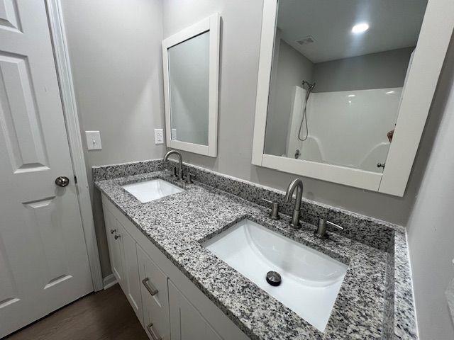 bathroom featuring double vanity, wood finished floors, a shower, and a sink