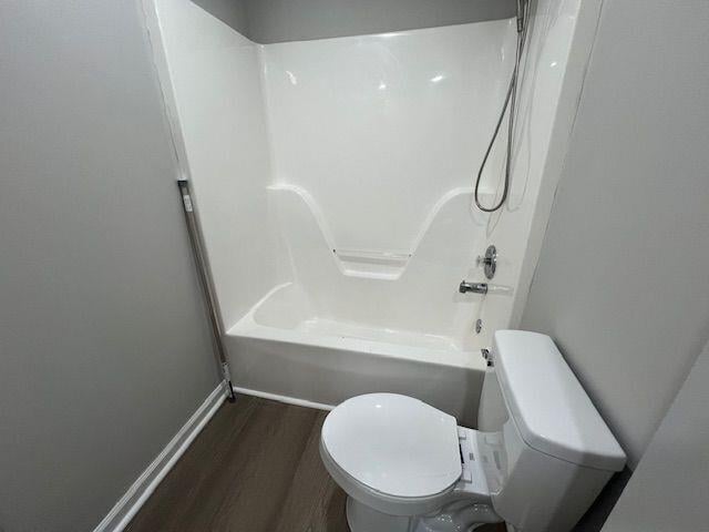 bathroom featuring toilet, shower / tub combination, wood finished floors, and baseboards