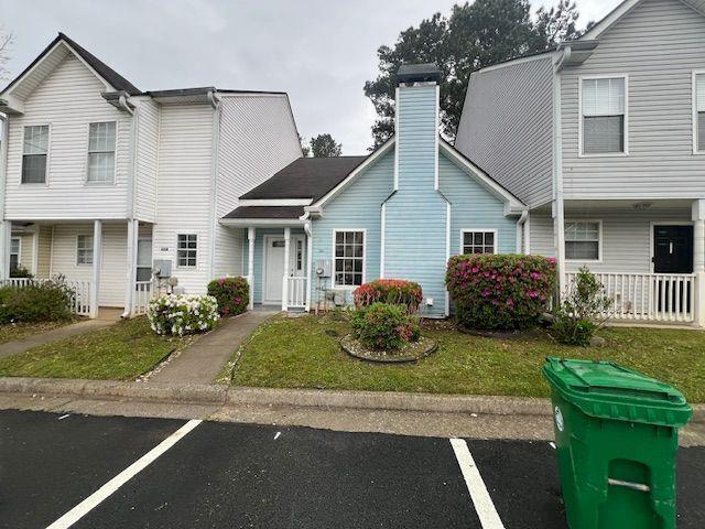 townhome / multi-family property with uncovered parking, a front lawn, and a chimney