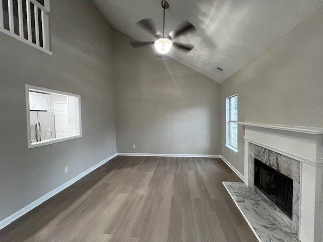 unfurnished living room with a premium fireplace, baseboards, wood finished floors, a ceiling fan, and high vaulted ceiling