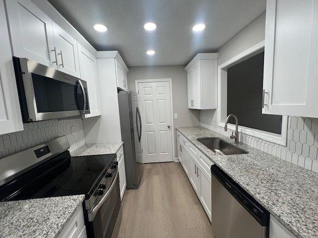 kitchen featuring light wood finished floors, a sink, stainless steel appliances, backsplash, and white cabinetry
