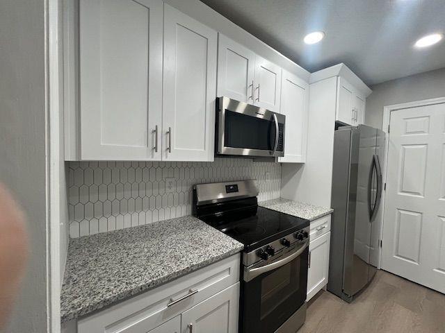 kitchen with light stone countertops, decorative backsplash, light wood-style flooring, white cabinets, and appliances with stainless steel finishes