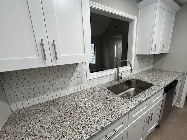 kitchen with white cabinetry, tasteful backsplash, light stone counters, and a sink
