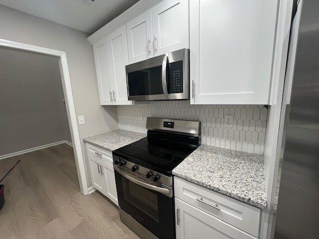 kitchen featuring appliances with stainless steel finishes, tasteful backsplash, light wood-style flooring, and white cabinets