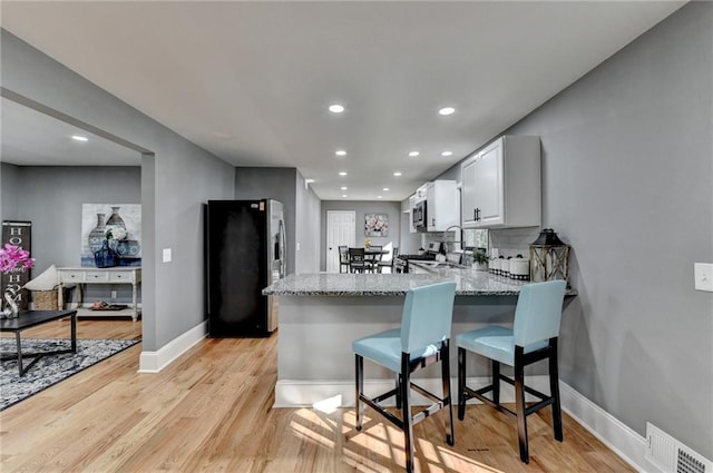 kitchen featuring light stone countertops, appliances with stainless steel finishes, white cabinetry, kitchen peninsula, and a breakfast bar area