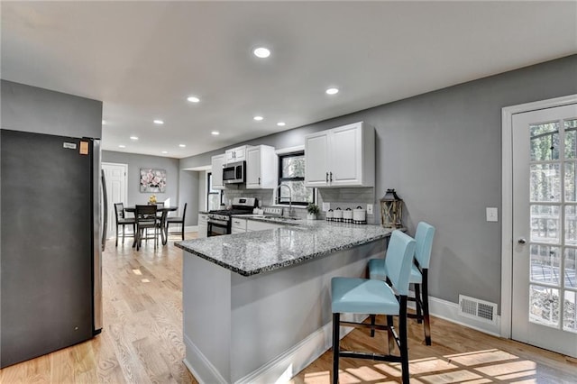 kitchen featuring white cabinetry, light stone countertops, a kitchen breakfast bar, kitchen peninsula, and appliances with stainless steel finishes