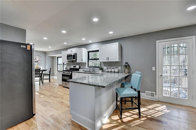 kitchen featuring white cabinets, a kitchen breakfast bar, stone countertops, kitchen peninsula, and stainless steel appliances