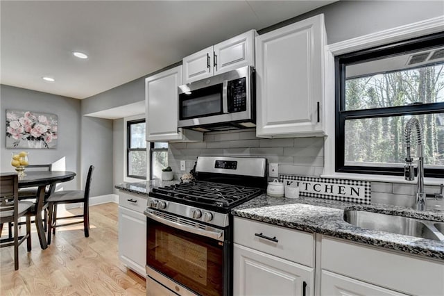 kitchen featuring appliances with stainless steel finishes, tasteful backsplash, sink, dark stone countertops, and white cabinets