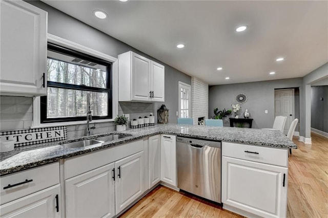 kitchen with kitchen peninsula, decorative backsplash, stainless steel dishwasher, sink, and white cabinets