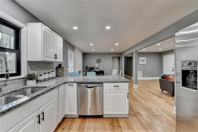 kitchen featuring stainless steel appliances, tasteful backsplash, light stone counters, kitchen peninsula, and white cabinets