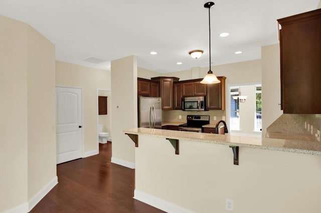 kitchen featuring kitchen peninsula, a breakfast bar, dark wood-type flooring, pendant lighting, and stainless steel appliances