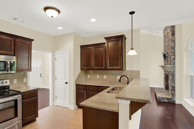 kitchen featuring kitchen peninsula, stainless steel appliances, sink, light hardwood / wood-style floors, and decorative light fixtures