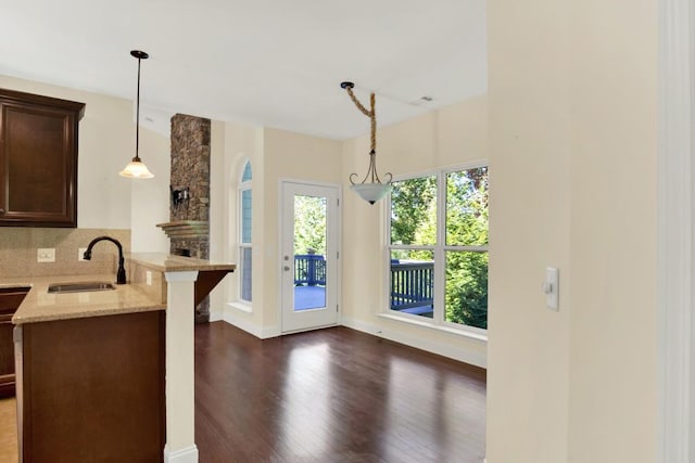 kitchen featuring tasteful backsplash, light stone countertops, dark wood-type flooring, pendant lighting, and sink