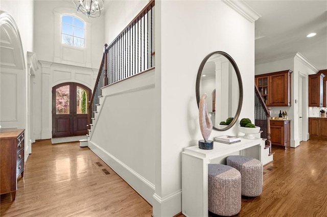 entryway with a chandelier, crown molding, light wood finished floors, stairs, and a high ceiling