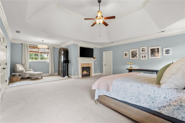 carpeted bedroom featuring a tray ceiling, a warm lit fireplace, baseboards, visible vents, and ornamental molding