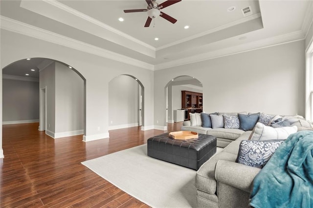 living area featuring a ceiling fan, a raised ceiling, wood finished floors, baseboards, and a healthy amount of sunlight