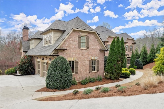 view of home's exterior featuring fence, a chimney, concrete driveway, brick siding, and a shingled roof