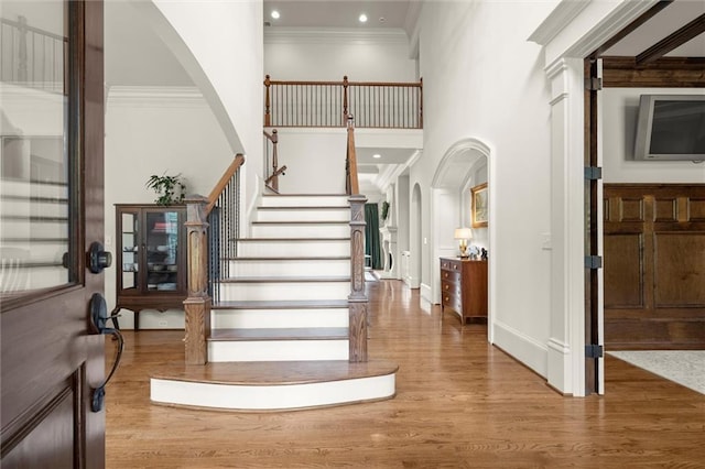 entryway with crown molding, a towering ceiling, wood finished floors, stairway, and arched walkways