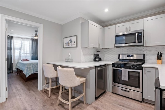 kitchen with light wood-style flooring, appliances with stainless steel finishes, light countertops, and ornamental molding