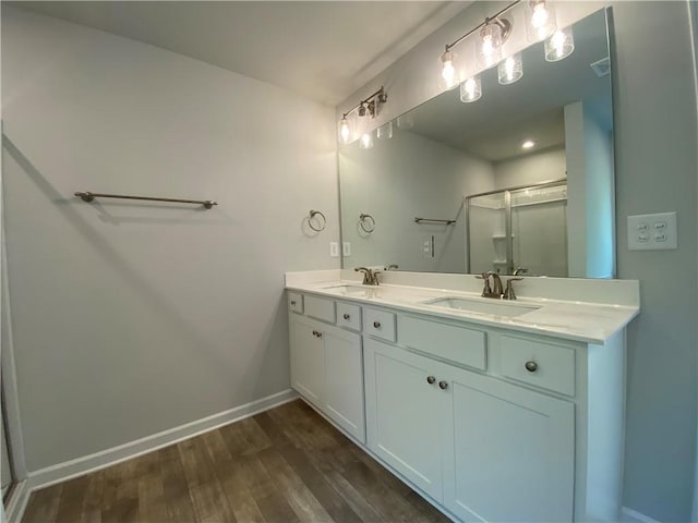 bathroom featuring a stall shower, wood finished floors, double vanity, and baseboards
