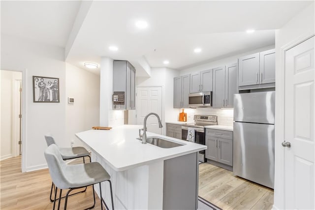 kitchen with a breakfast bar area, light countertops, gray cabinetry, appliances with stainless steel finishes, and a sink