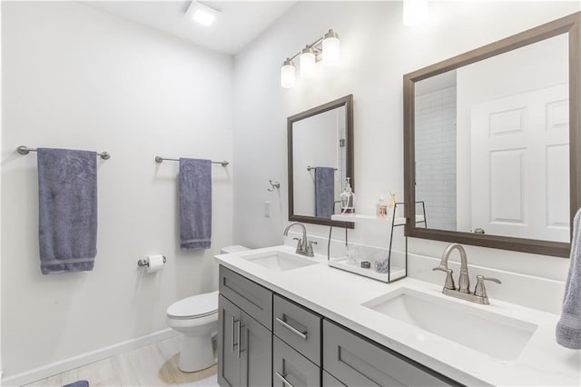 bathroom featuring toilet, double vanity, baseboards, and a sink