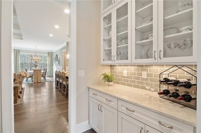 bar featuring light stone counters, wood-type flooring, ornamental molding, decorative backsplash, and white cabinets