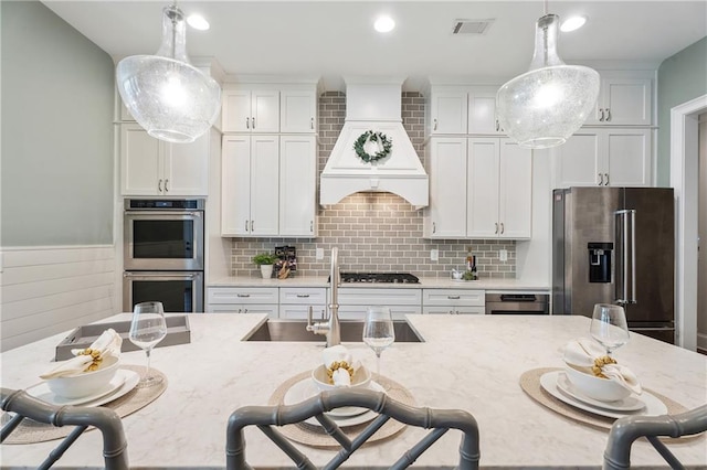 kitchen featuring premium range hood, stainless steel appliances, light stone countertops, and pendant lighting