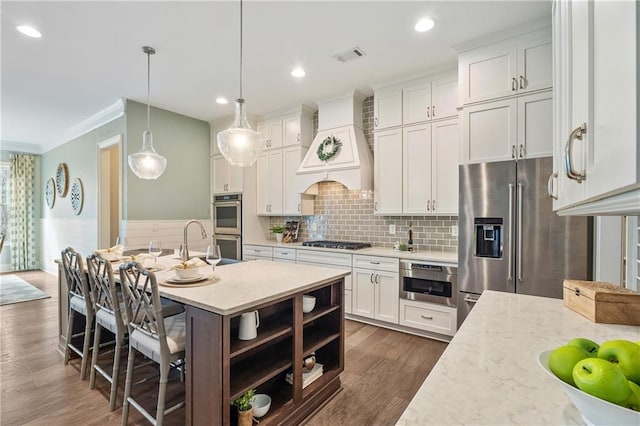 kitchen featuring white cabinetry, stainless steel appliances, light stone countertops, custom range hood, and decorative light fixtures