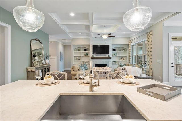 kitchen featuring coffered ceiling, sink, hanging light fixtures, a large fireplace, and built in features