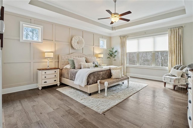 bedroom with crown molding, ceiling fan, a raised ceiling, and multiple windows